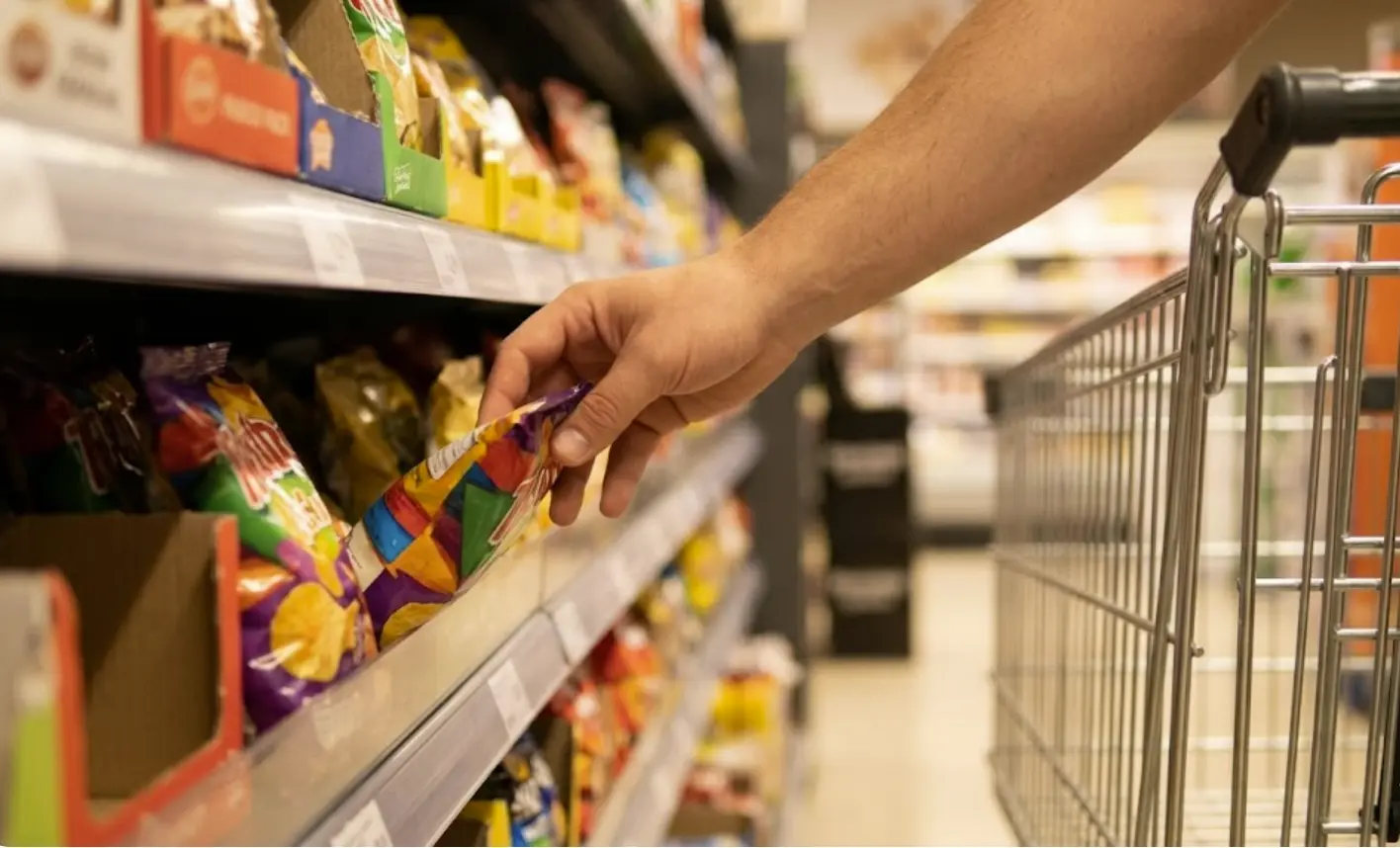 Mano alcanzando producto de forma impulsiva en supermercado, ejemplo de compra por hambre